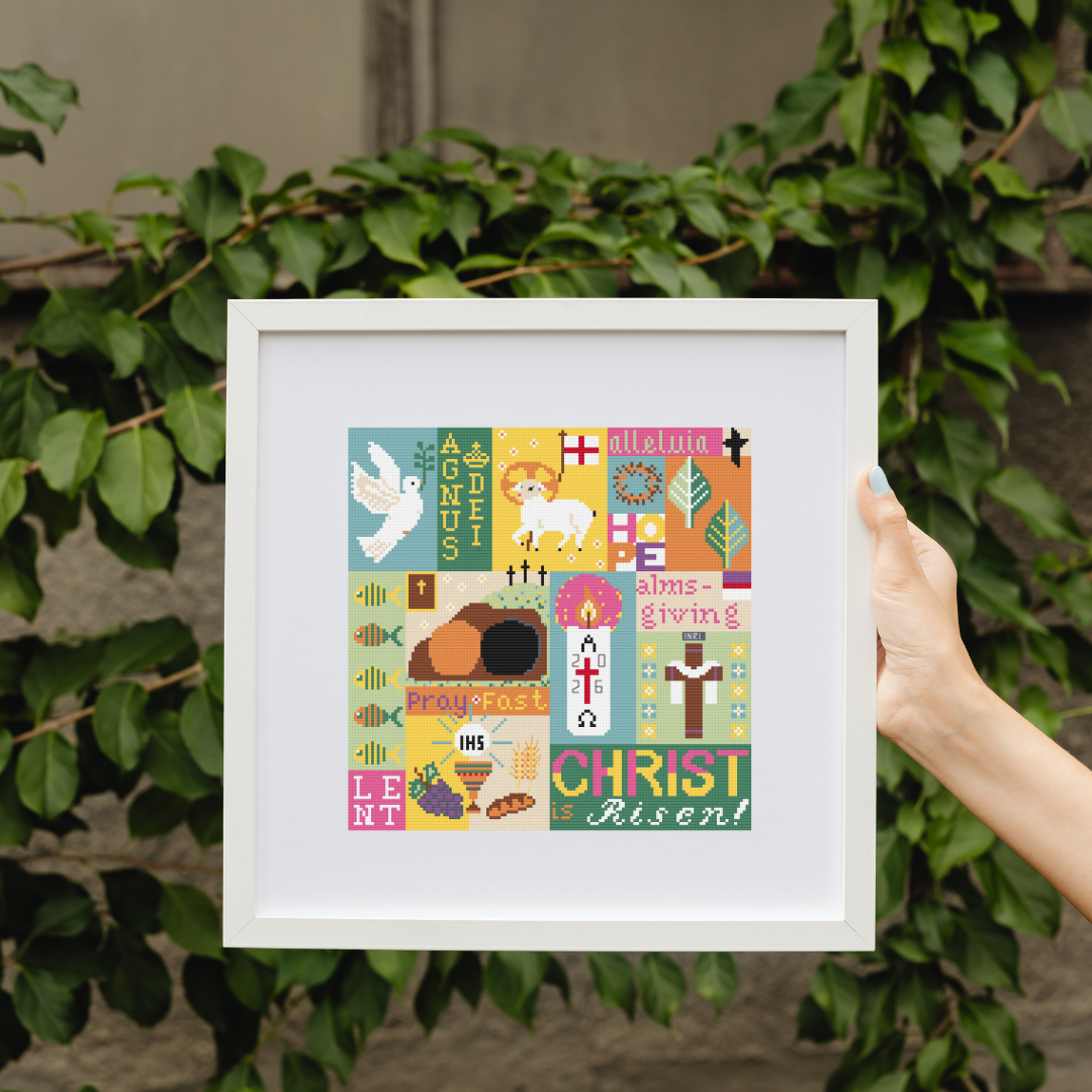 Catholic Easter Sampler Cross Stitch Completed Catholic Easter Sampler Cross Stitch in a white square frame held against a green leafy background